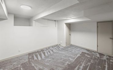 Empty basement room with gray carpet and white walls.