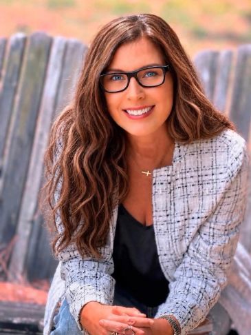 Smiling woman with glasses sitting outdoors.
