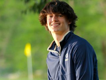 Young man smiling outdoors with a blurred green background.