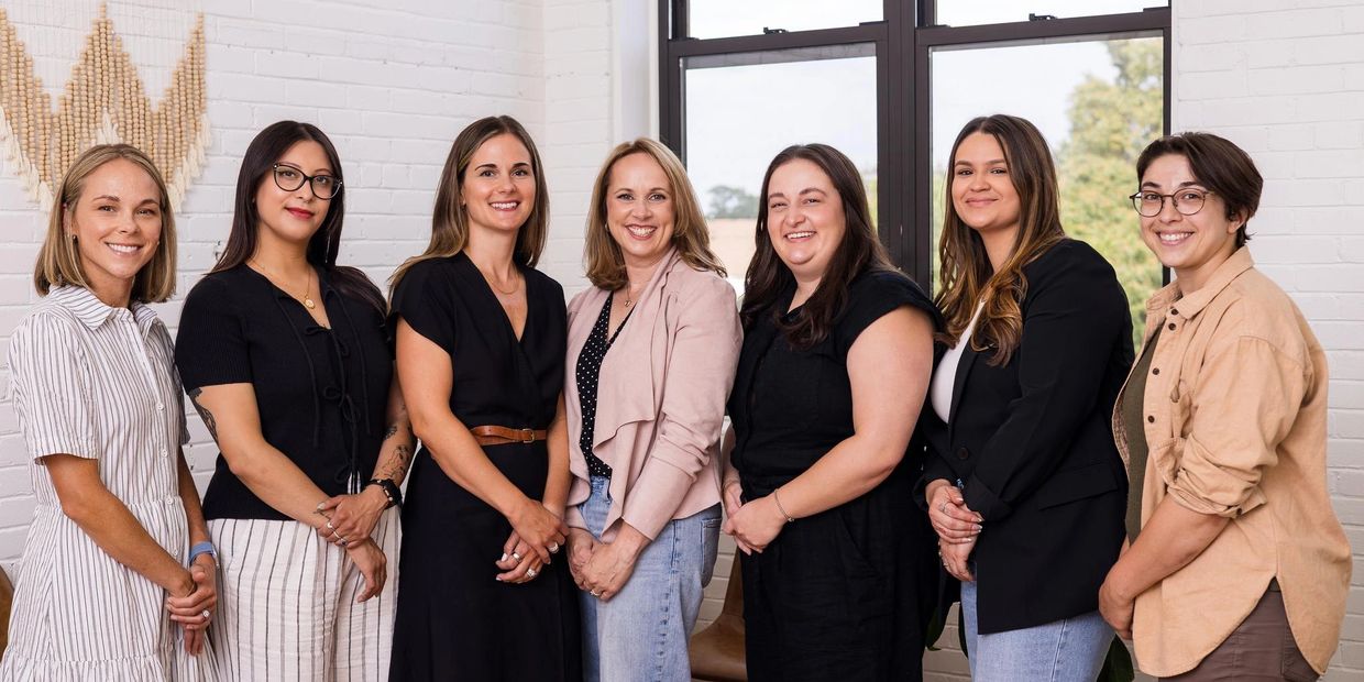Group of seven smiling women standing together indoors.
