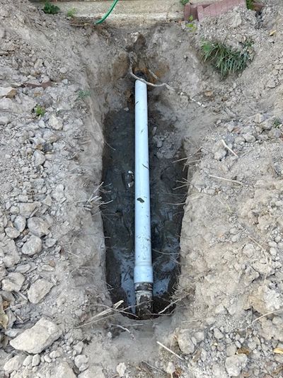 A trench with a white PVC pipe installed underground.