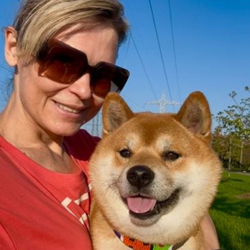 Woman in sunglasses holding a happy Shiba Inu dog outdoors.