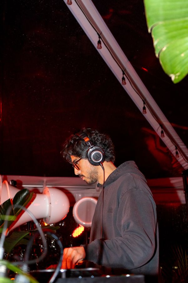 A DJ wearing headphones performs at a night event with red lighting.