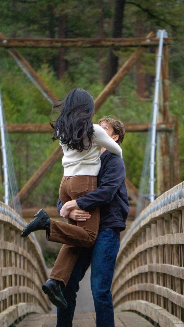 Couple embraces joyfully on a wooden bridge surrounded by greenery.