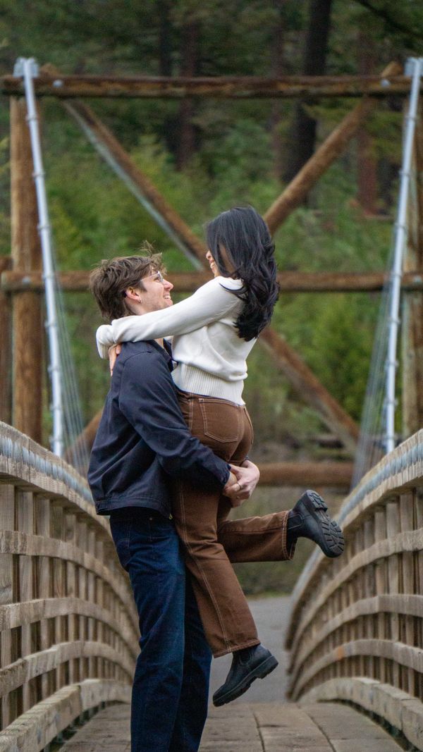 Couple embracing joyfully on a wooden bridge surrounded by nature.