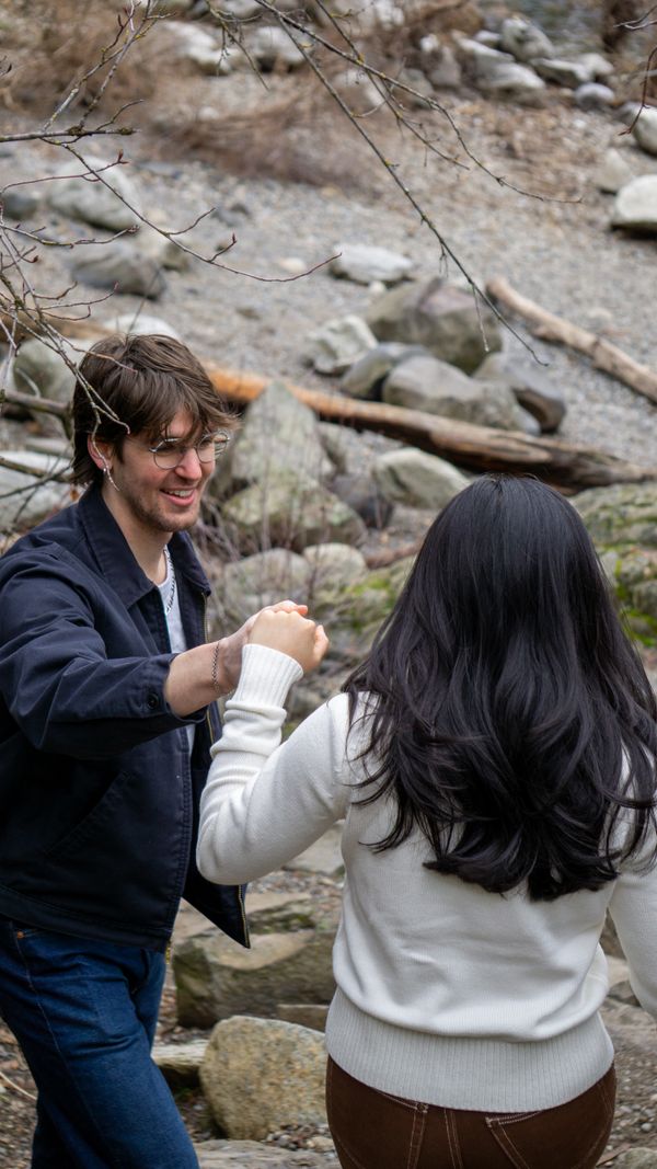A couple enjoying a playful moment outdoors among rocks and trees.