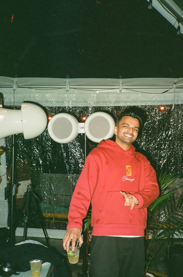A smiling man in a red hoodie holding a drink at a night event.