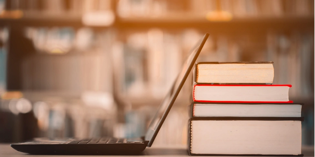 Laptop with books stacked up behind it