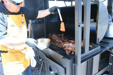 Chef basting meat on a large outdoor grill or smoker.