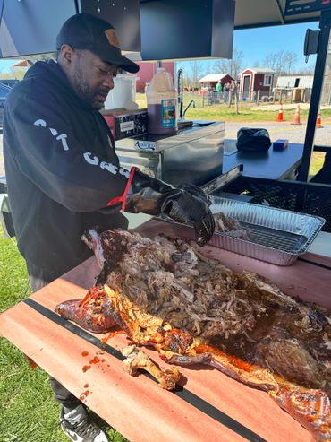 Man preparing pulled pork barbecue outdoors at a food stall.