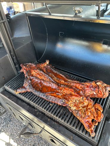 Whole roasted pig cooking on a large outdoor grill.