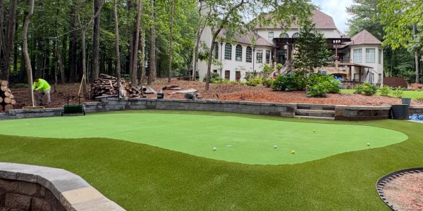 A putting green in a backyard with a house and worker.