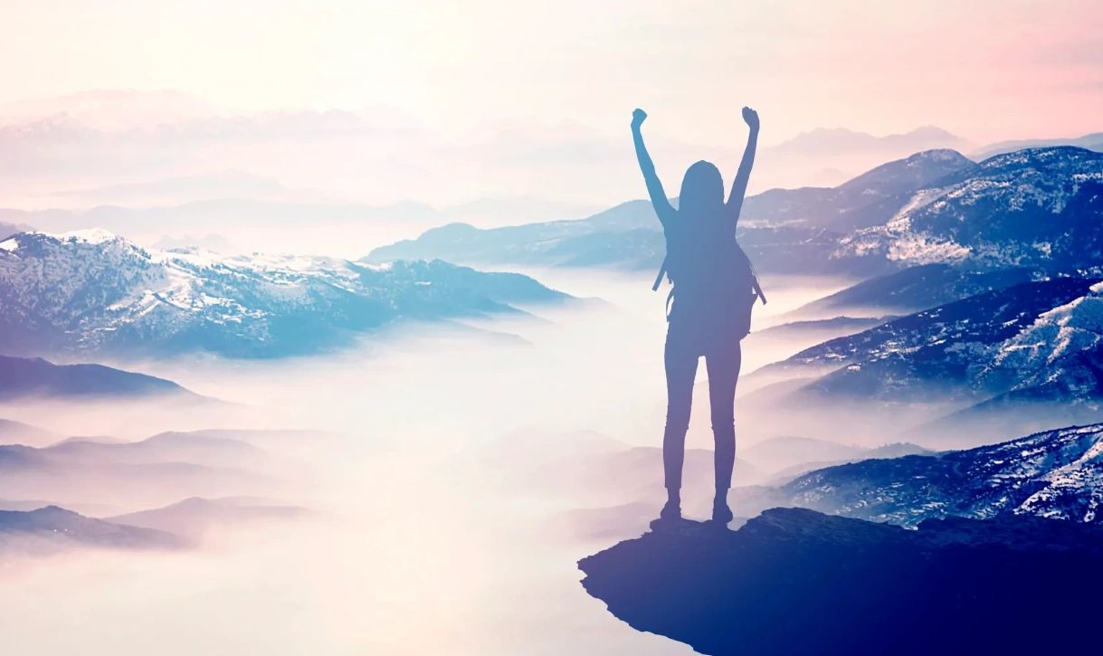 Silhouette of a person celebrating on a mountain peak above misty valleys.