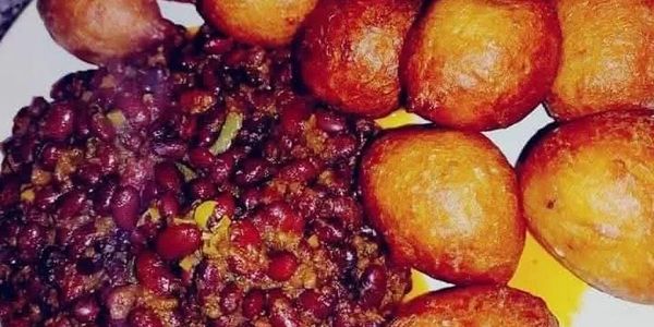 Fried dough balls served with a spicy bean stew on a white plate.