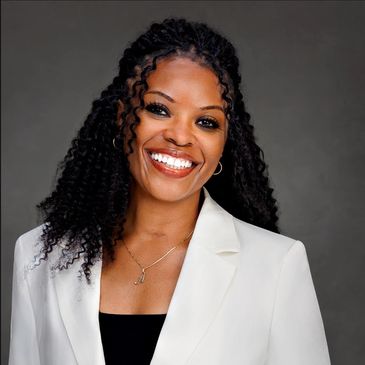 Smiling woman in white blazer with curly hair.