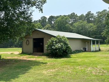 A metal barn surrounded by green grass and trees under a clear sky.