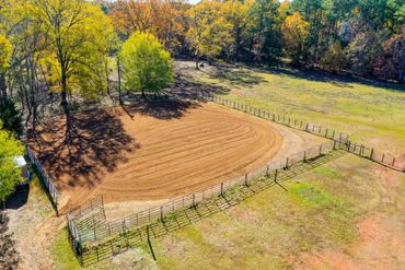 A fenced dirt paddock surrounded by trees with autumn foliage.
