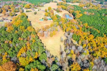 Aerial view of a countryside property surrounded by autumn trees and a small pond.