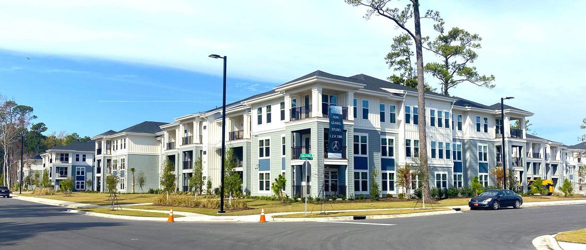 Modern apartment complex with leasing available, surrounded by trees and clear skies.