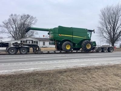 Large green combine harvester transported on a flatbed truck.