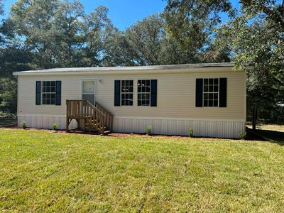 A beige mobile home with black shutters and a small wooden porch in a yard.