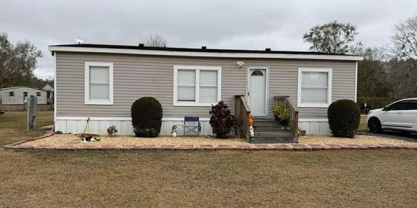 A beige mobile home with a small garden and a car parked beside it.