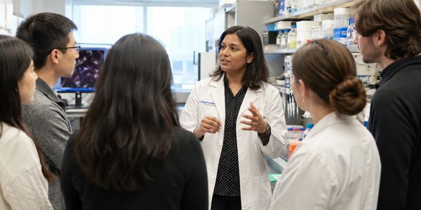 Scientist in lab coat explains research to attentive group in laboratory.