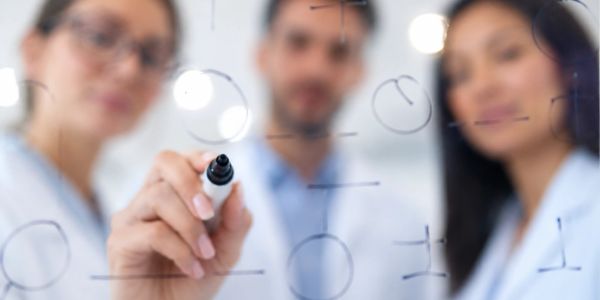 Three professionals writing on a transparent board with marker.