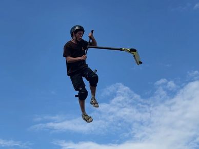 Pro Scooter rider jumping the box ramp at the skatepark