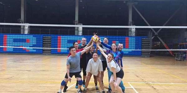 A joyful volleyball team poses together on an indoor court, holding up a volleyball.