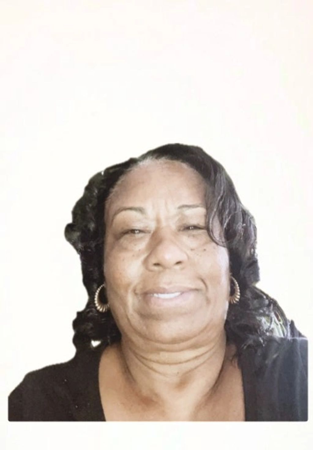 Smiling woman with curly hair and hoop earrings against a plain background.