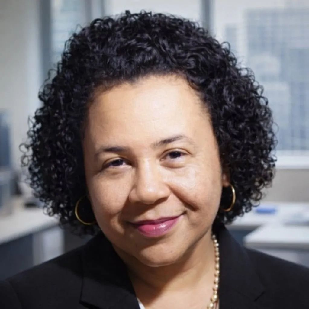Professional woman with curly hair and a warm smile in an office setting.