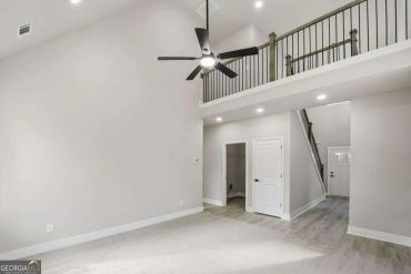 Empty modern living space with loft balcony and ceiling fan.