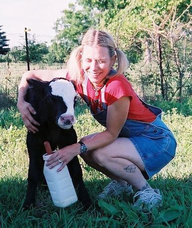 A woman smiles while feeding a calf outdoors on a sunny day.