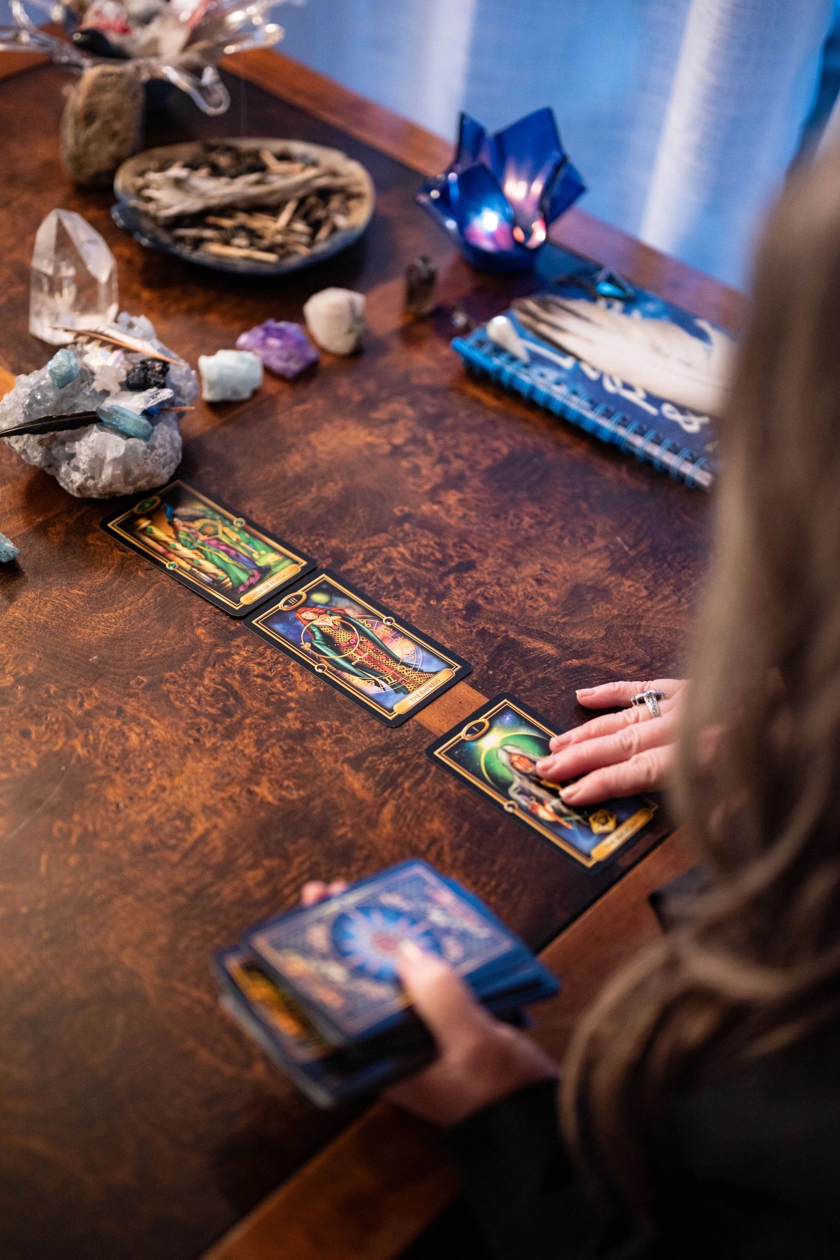 Nicolette laying out tarot cards on the dark, rich wood of a desk.