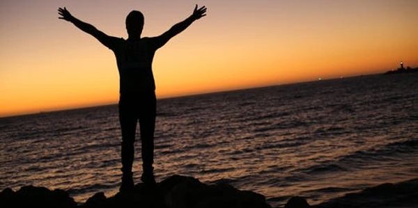 Person standing by ocean with arms wide open.