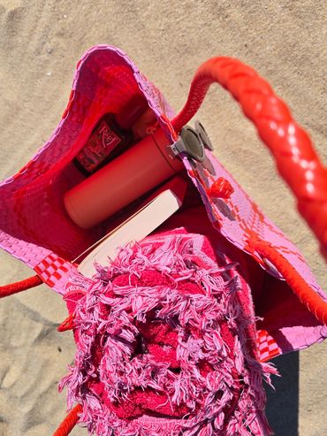 Open beach bag with a pink towel and essentials inside.