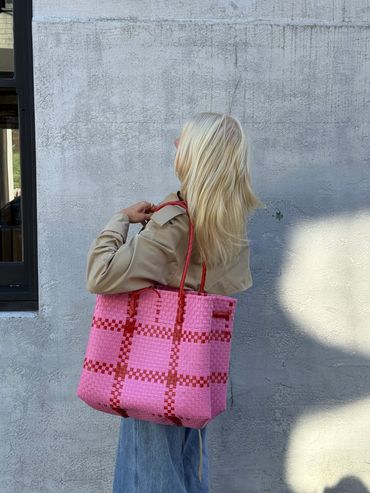 Person with blonde hair holding a large pink and red checkered tote bag.