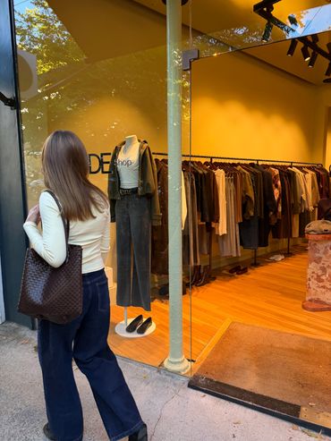 Woman with brown bag looking into a clothing store window.