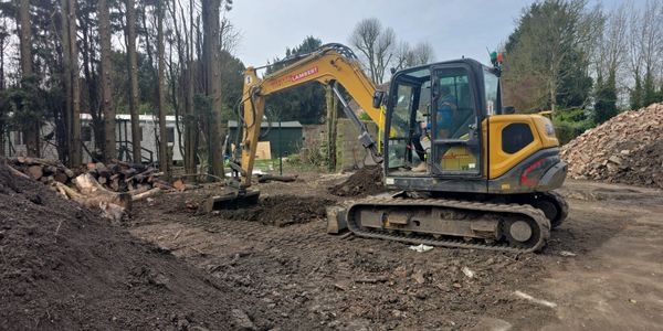 Yellow excavator digging soil at a construction site surrounded by trees.