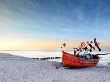 Orange fishing boat on a calm beach at sunset in Sopot