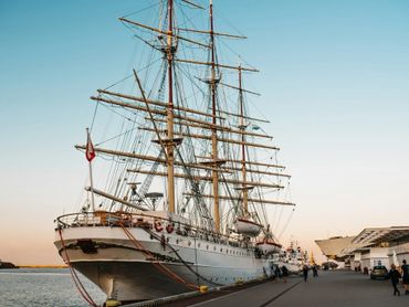 A large sailing ship  docked at a harbour in Gdynia during sunset.