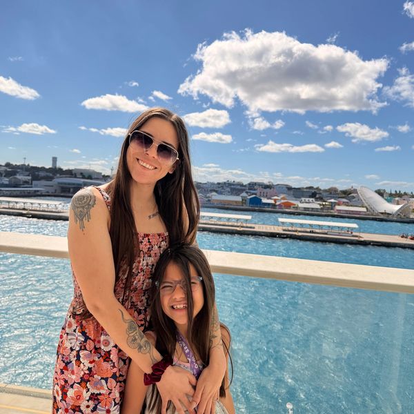 A smiling travel advisor hugs a happy young girl on a cruise vacation.