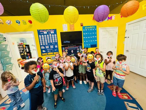 Children in a colorful classroom holding smiley face masks.