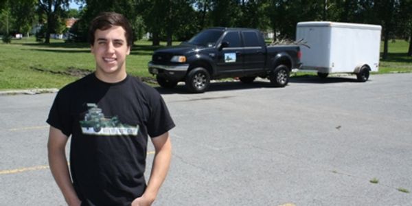 Young man smiling in front of a black pickup truck with a trailer.