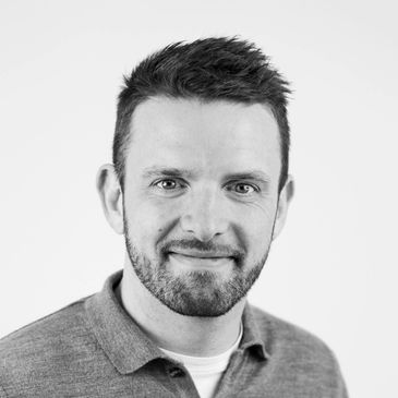 Black and white portrait of a smiling man with a beard and short hair.