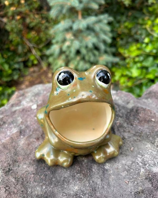 A ceramic frog with big eyes and open mouth on a rock.