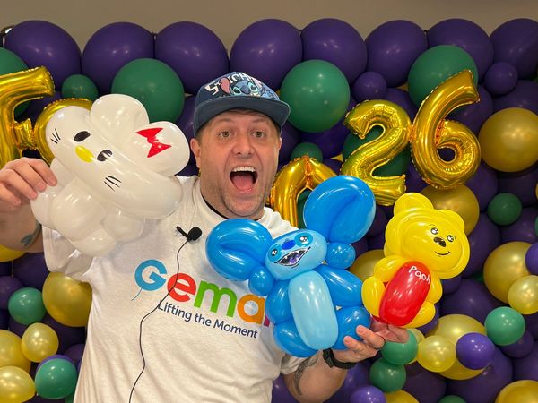 Man holding balloon animals, excited at a colorful party.