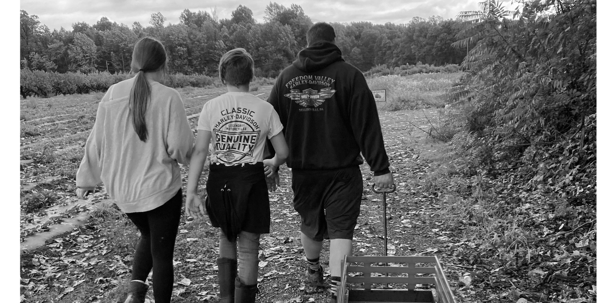 Caleb pulling a wagon and walking through a pumpkin patch with his two children.