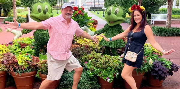 man and woman pose in front of a mickey and Minnie topiary at Walt disney world